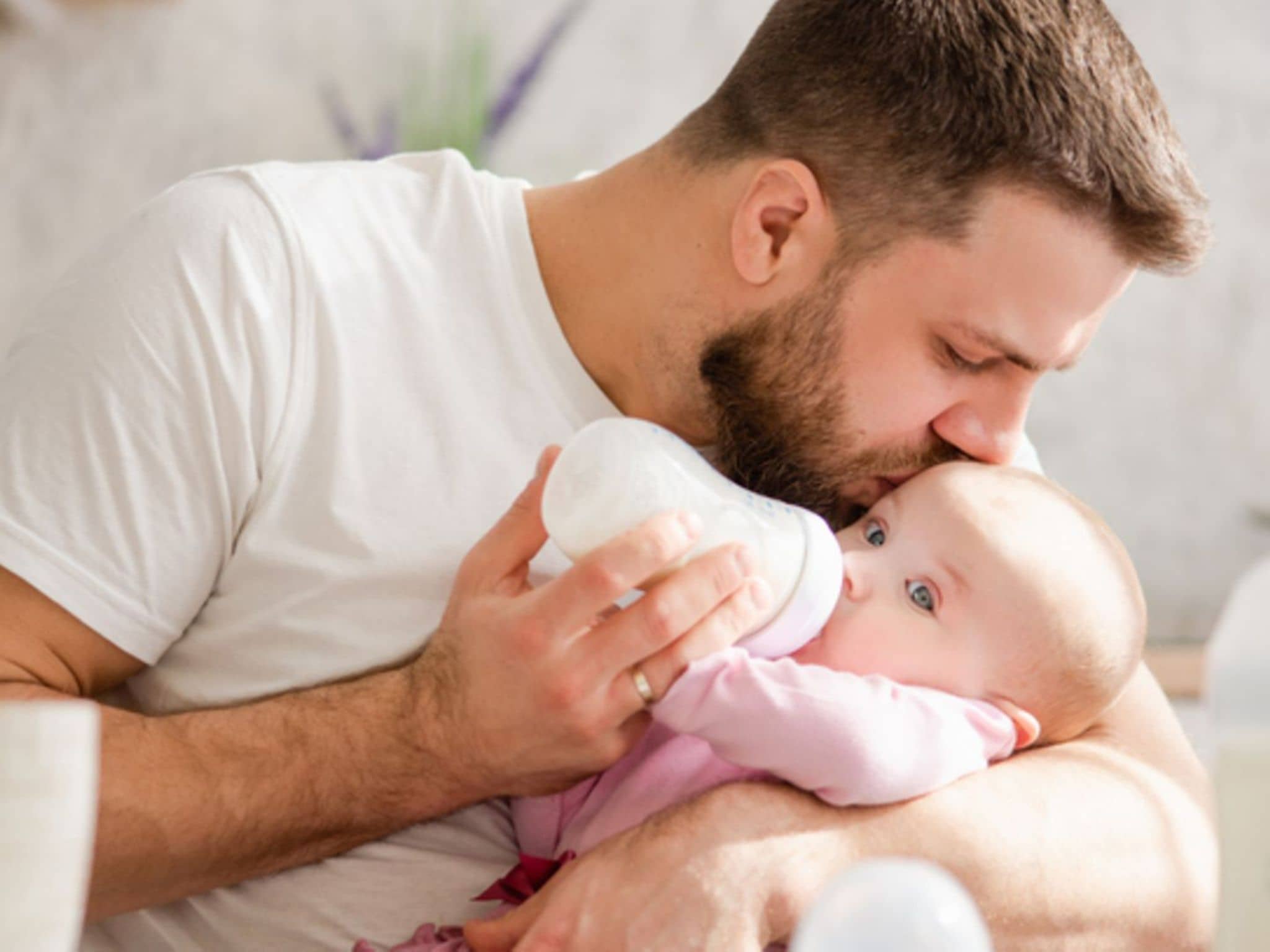 Säuglingsmilchnahrung: Vater küsst Baby beim Füttern mit der Flasche auf die Stirn
