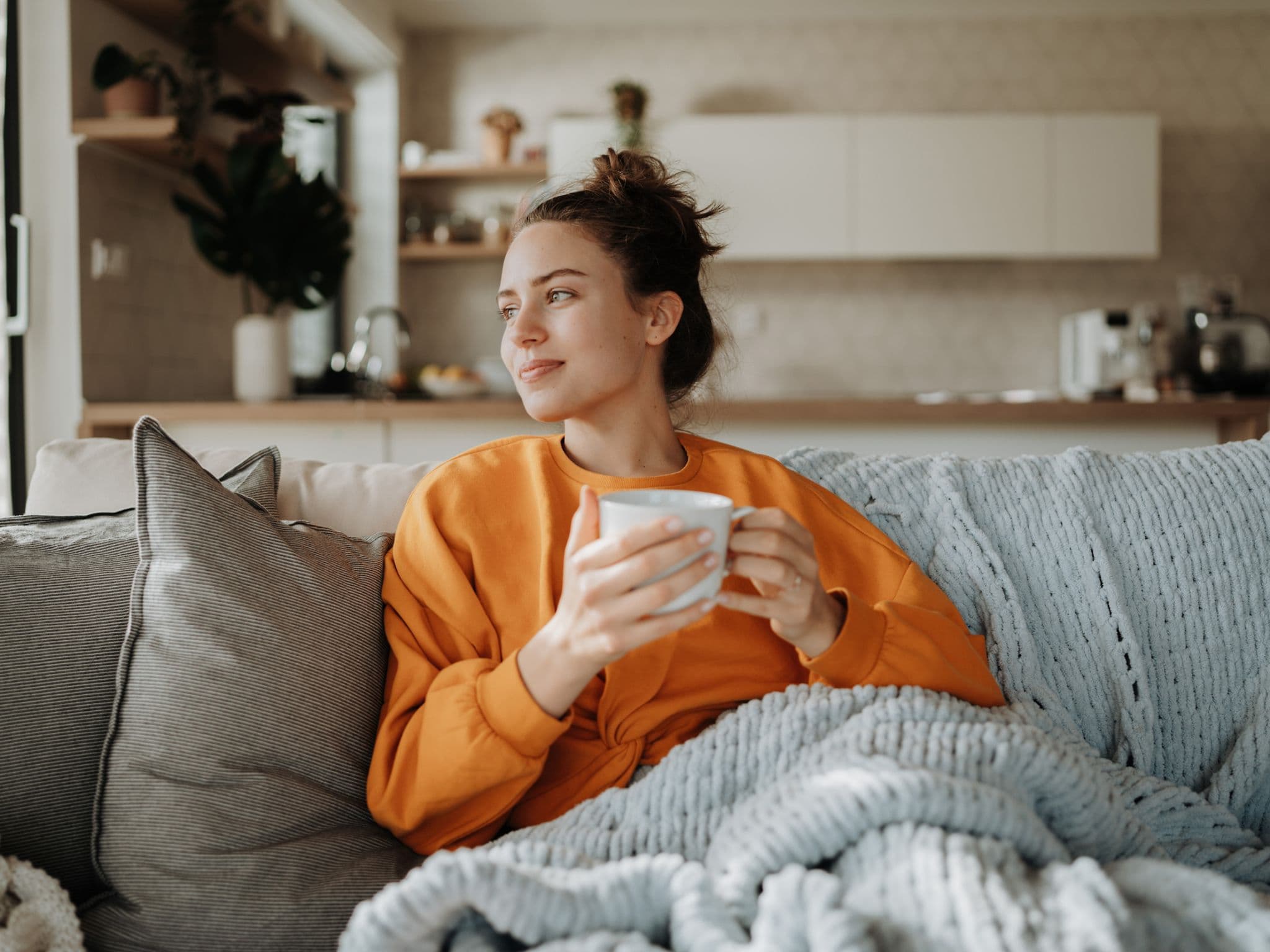Herzförmige Gebärmutter: Eine junge Frau sitzt gemütlich auf einem Sofa und hält einen Becher in der Hand