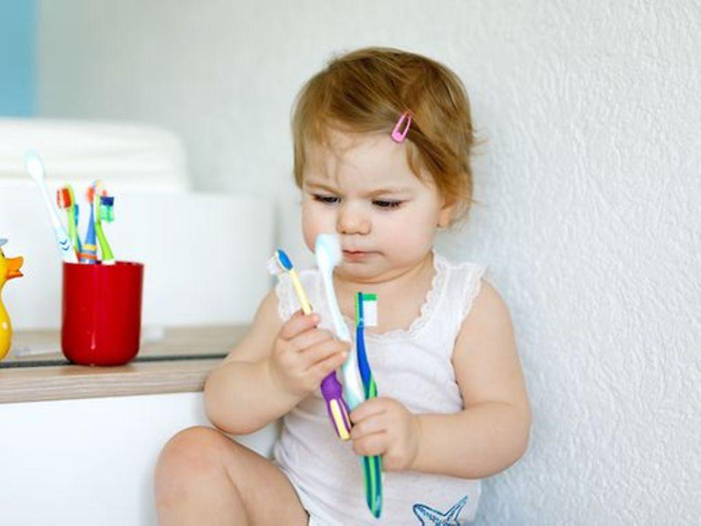 Kreidezähne bei Kindern: Ein kleines Mädchen beäugt Zahnbürsten in ihren Händen