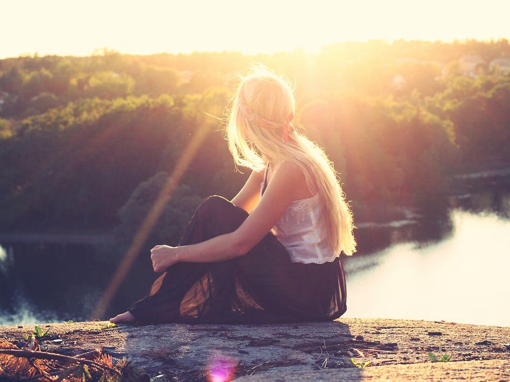 Erfüllter leben: Eine Frau sitzt auf einem Berg in der Sonne und genießt den weiten Blick