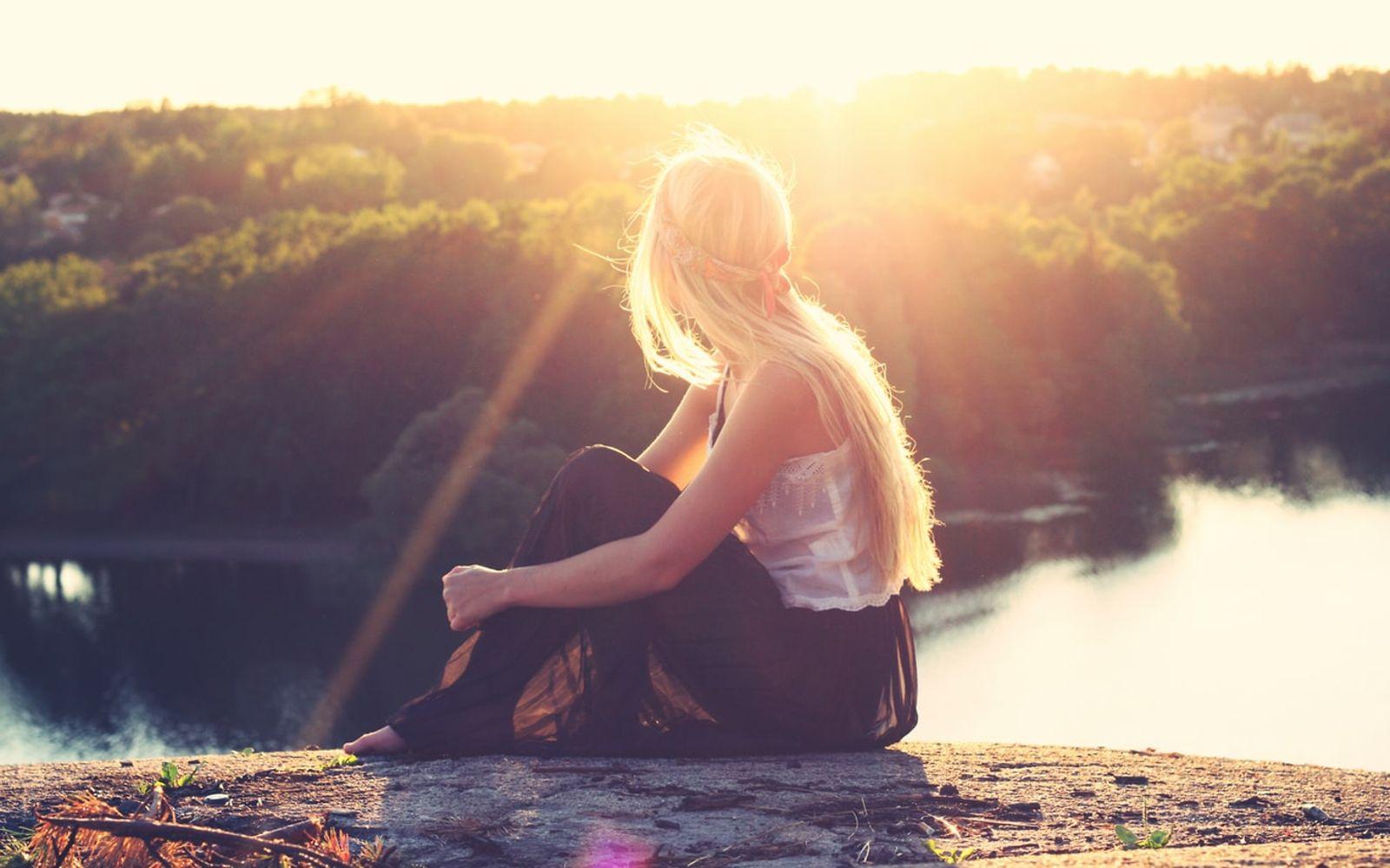 Erfüllter leben: Eine Frau sitzt auf einem Berg in der Sonne und genießt den weiten Blick