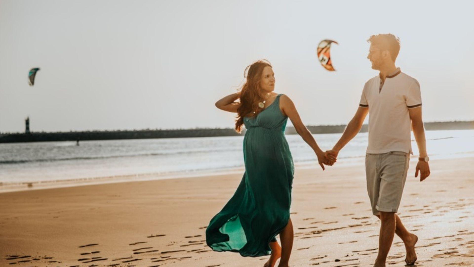 Fliegen in der Schwangerschaft: Schwangere und Mann laufen Hand in Hand am Strand entlang