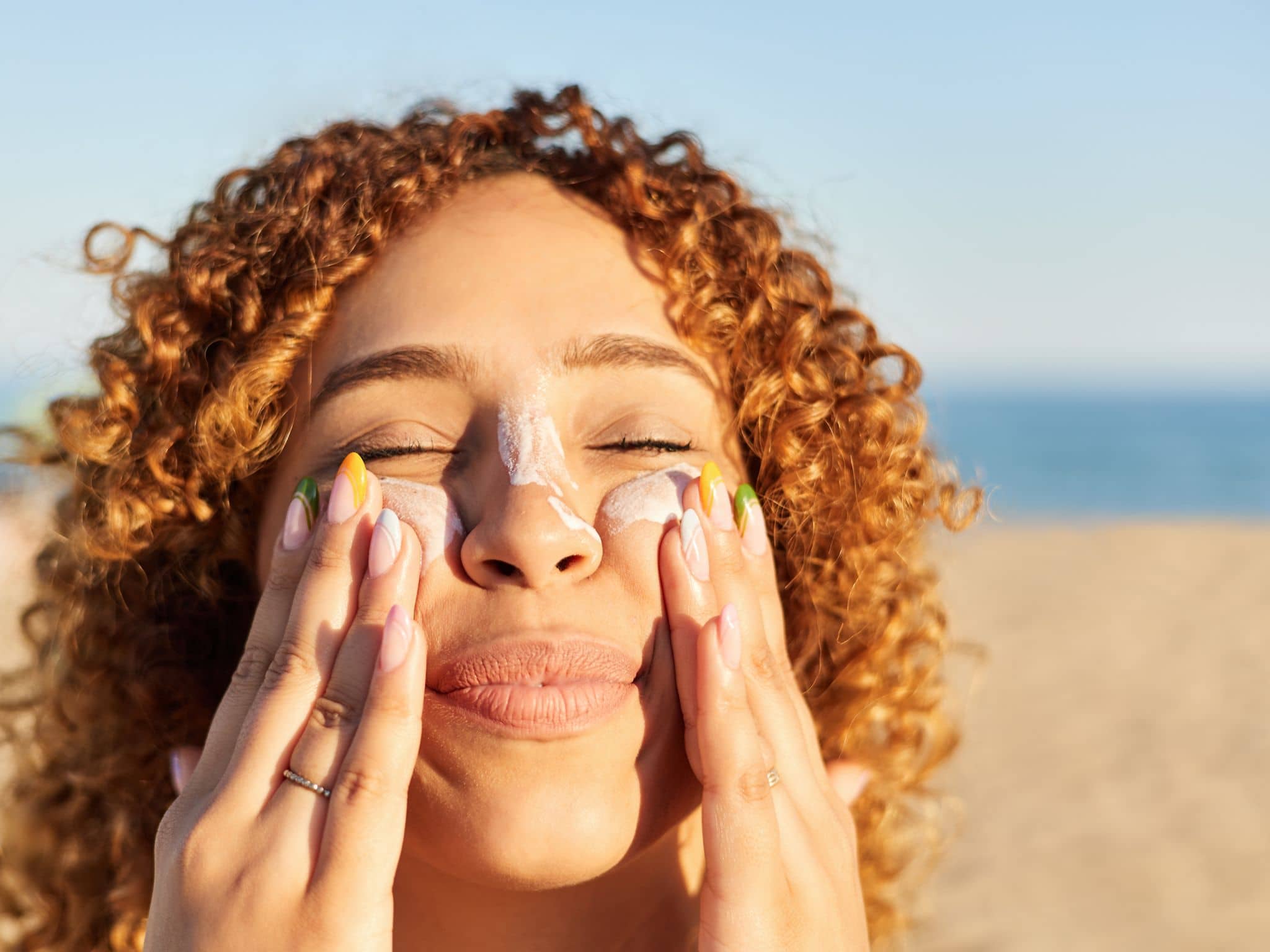 Lichtschutzfaktor: Frau am Strand cremt sich mit Sonnencreme am Strand das Gesicht ein.