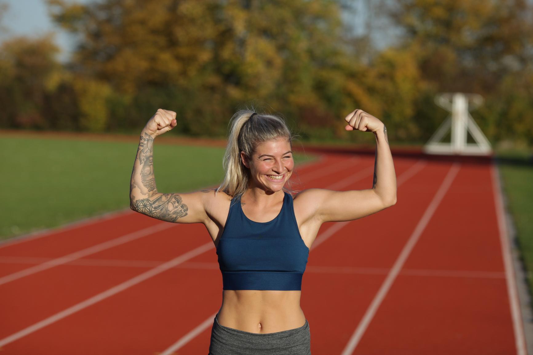 Massagepistole: Athletische Frau zeigt ihre Muskeln auf dem Sportfeld