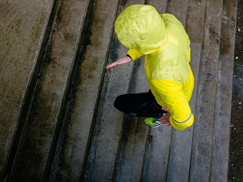 Wintermüdigkeit: Sportler in Regenkleidung läuft eine nasse Treppe hoch