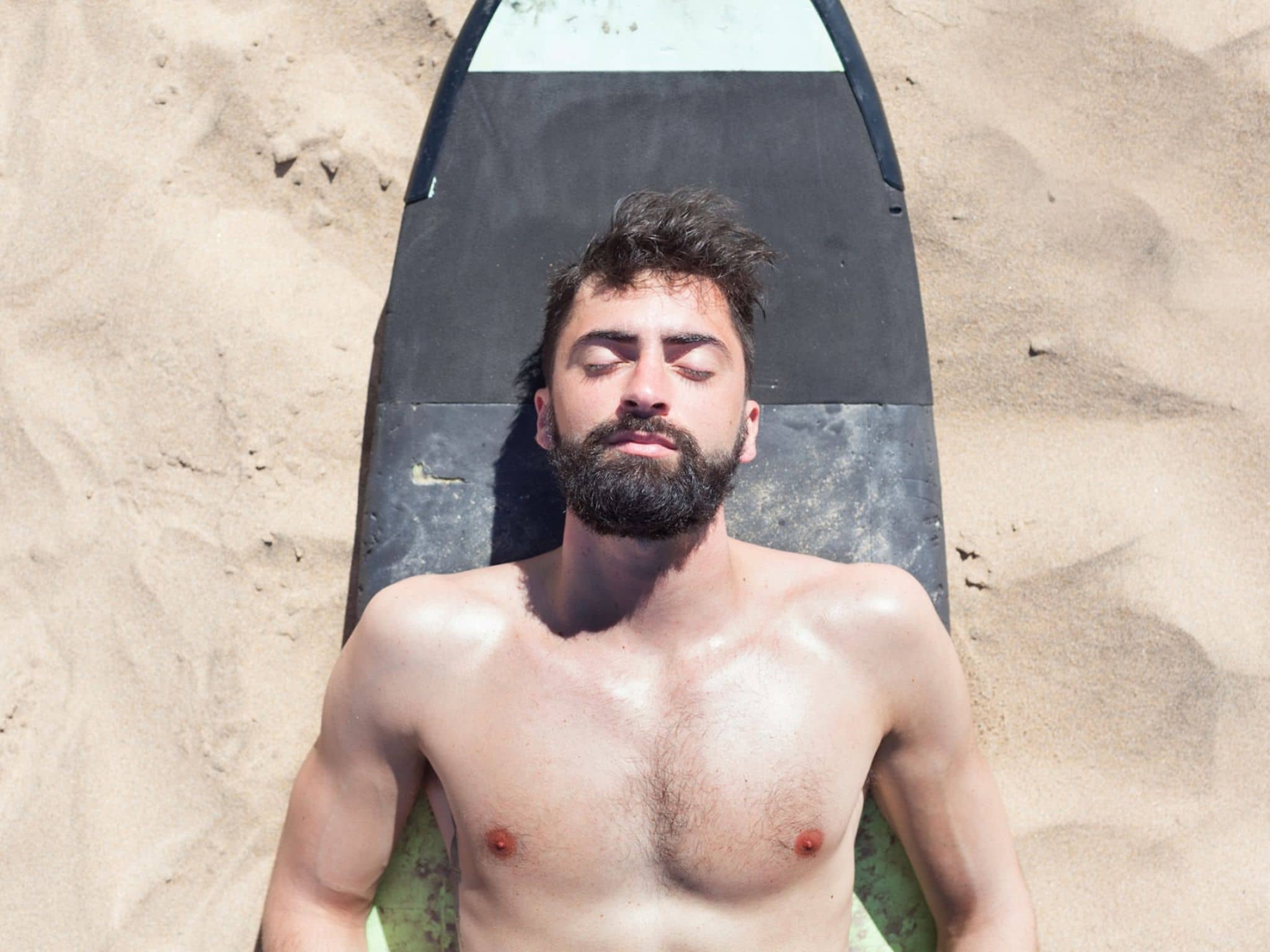 Hübscher Surfer entspannt sich am Strand