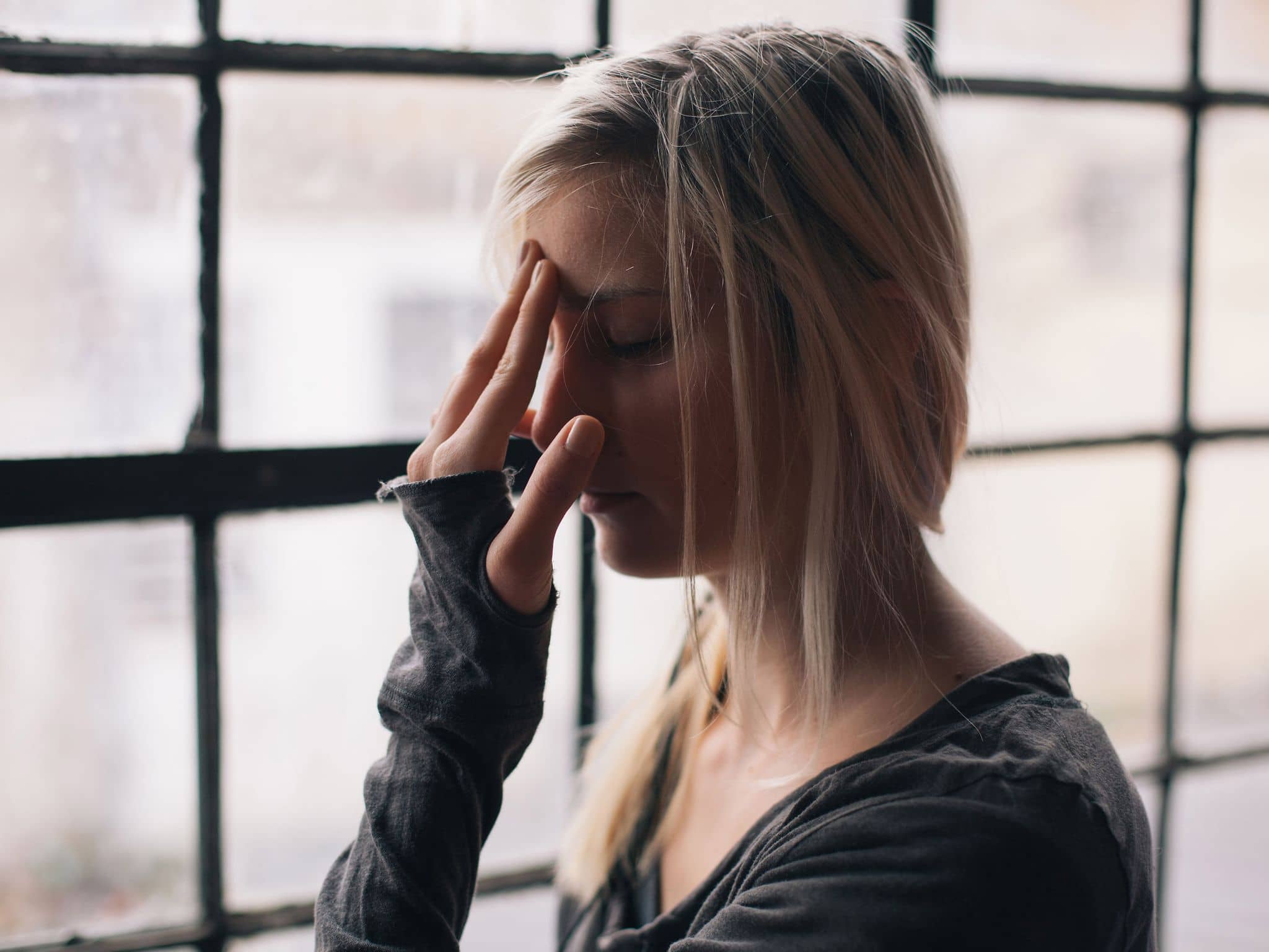 Schimmelpilzallergie: Frau mit geschlossenen Augen fässt sich mit einer Hand an die Stirn.