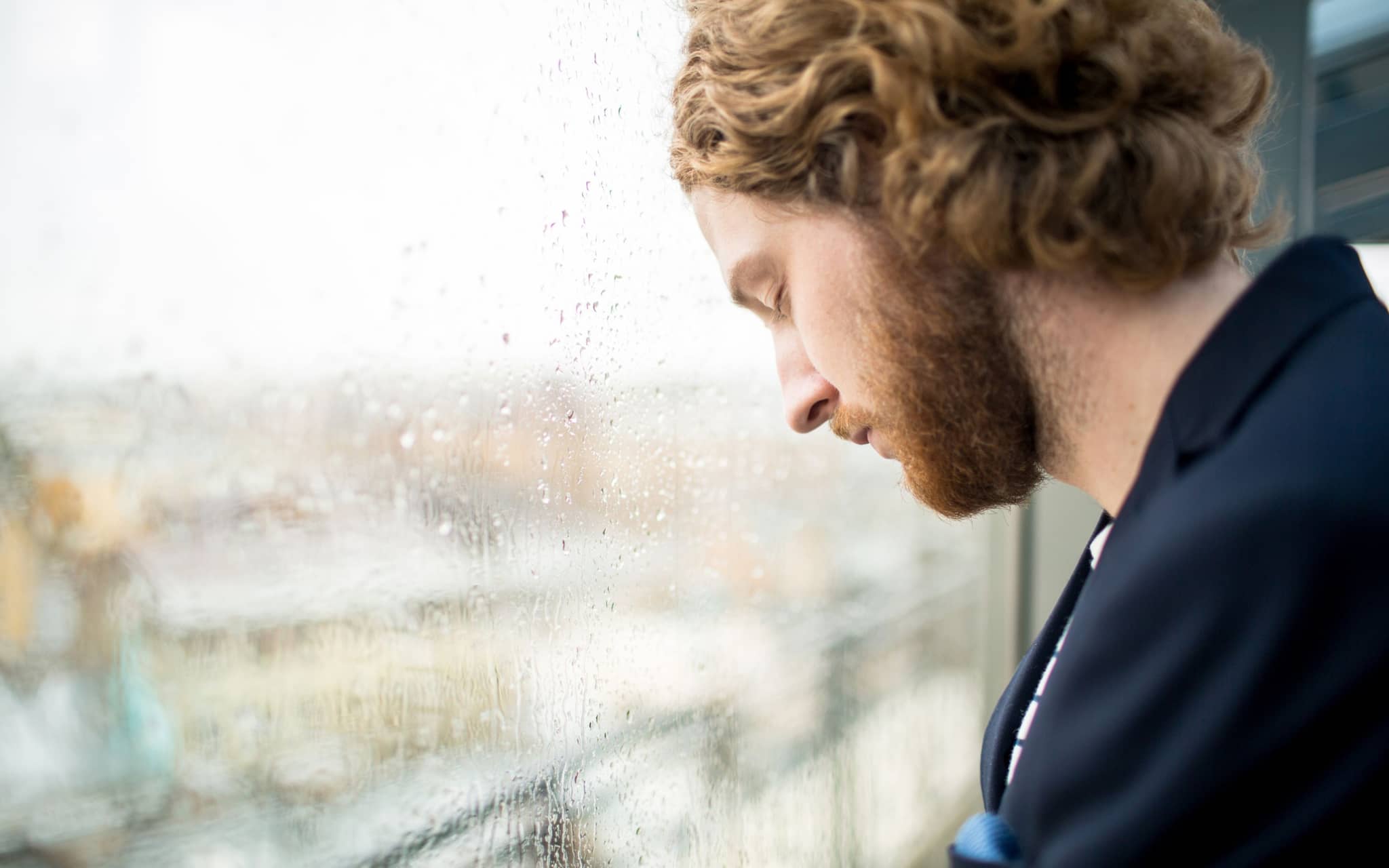 Bild: Trauriger Mann steht bei Regenwetter mit geschlossenen Augen am Fenster.