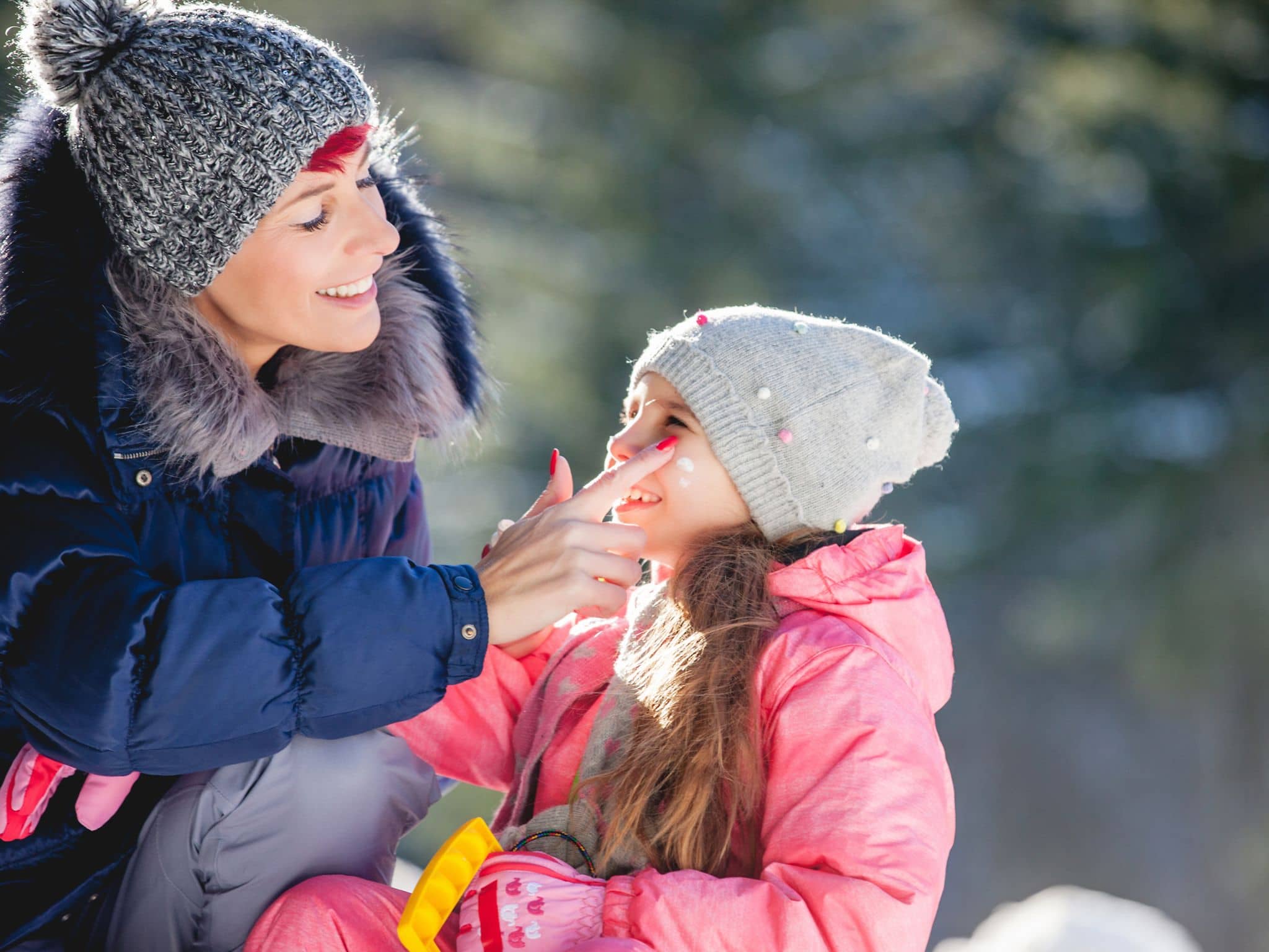 Hautpflege im Winter: Eine Frau cremt ein Kind mit Creme im Gesicht ein