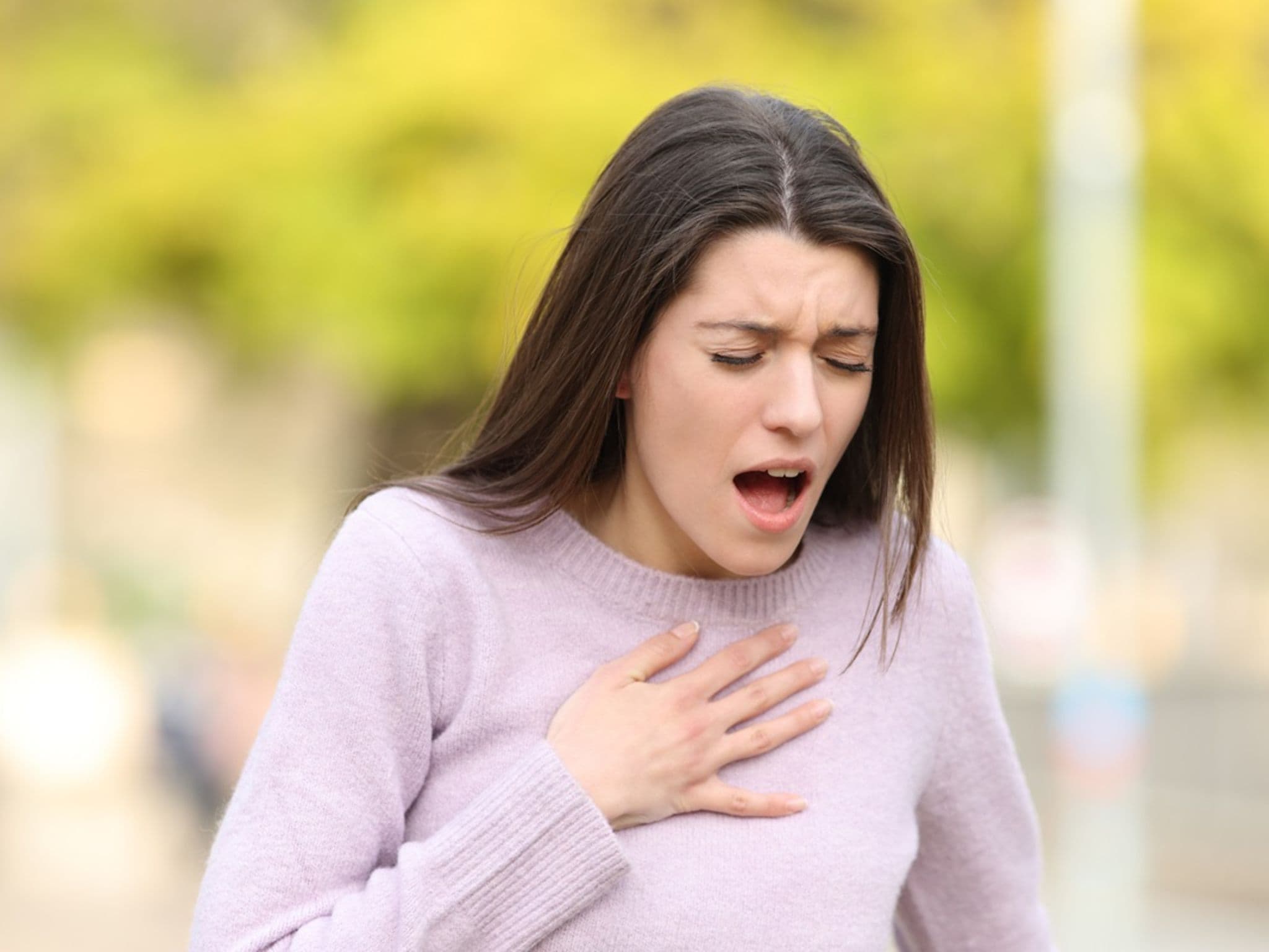 Frau mit Atemnot erlebt anaphylaktischen Schock und hält sich die Hand auf das Dekoletée.
