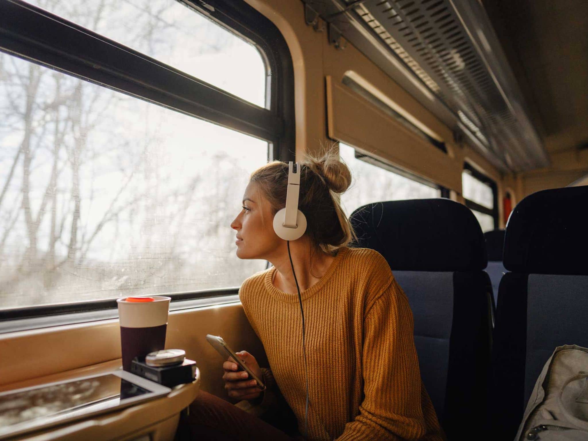 Junge Frau sitzt im Zug und hört über Kopfhörer Musik