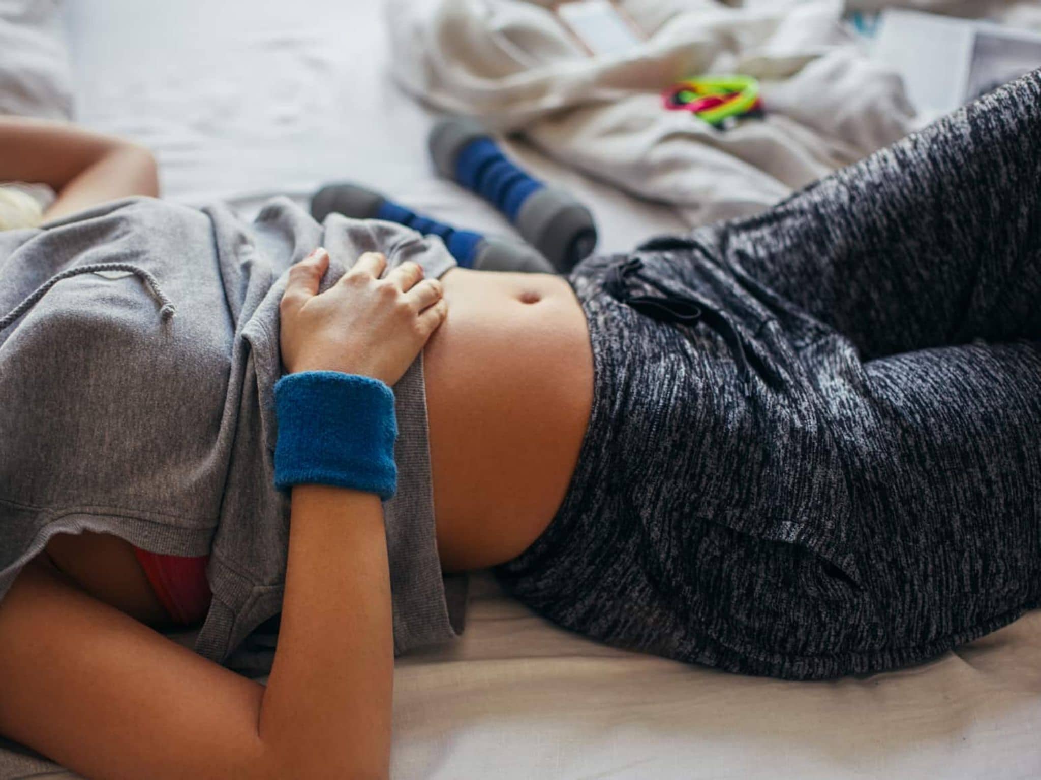 Sport bei Regelschmerzen: Frau in Sportkleidung, die sich auf ihrem Bett ausruht