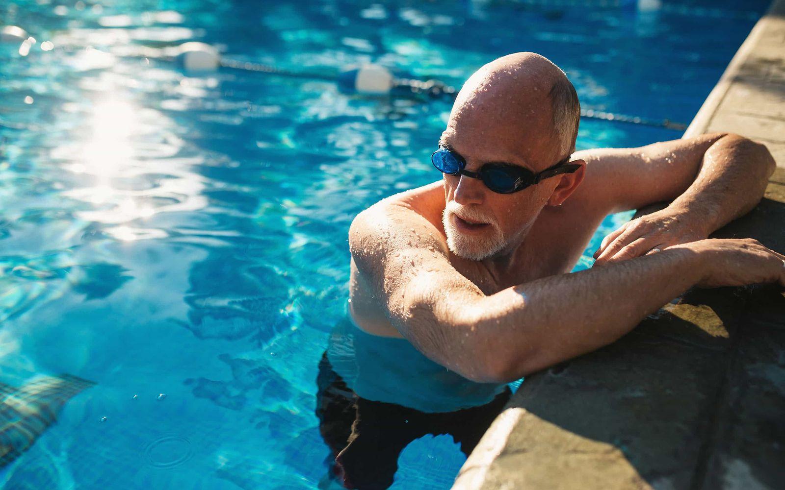 Herzinfarkt: Älterer Mann mit Schwimmbrille hält sich am Beckenrand eines  Schwimmbeckens fest.