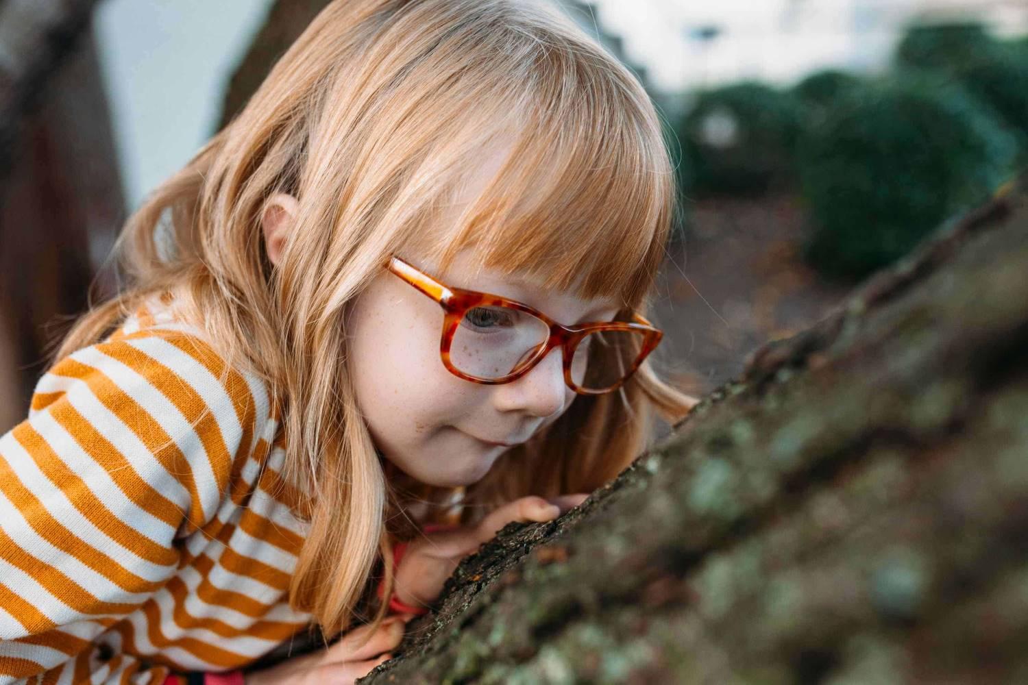 Hilfsmittel: Mädchen mit Brille betrachtet Baumrinde.