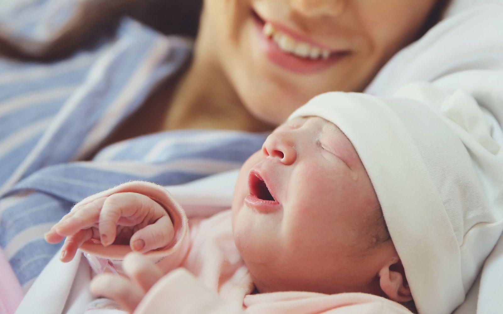 Arten der Geburt: Lächelnde Frau und Neugeborenes mit Mütze nebeneinander.