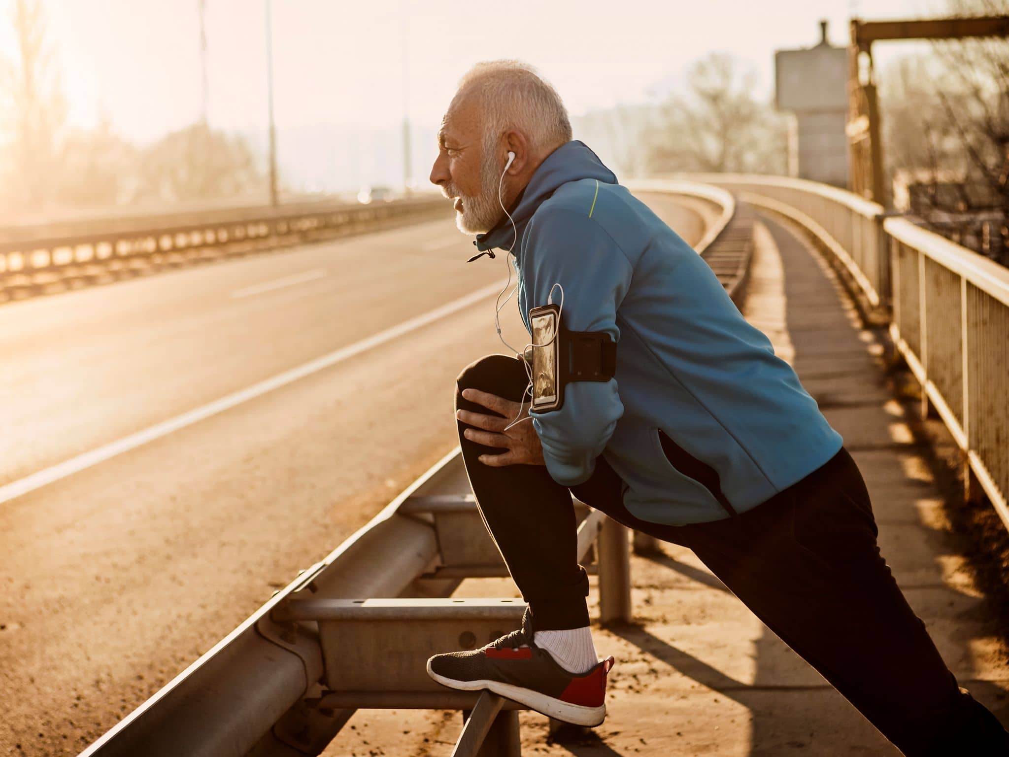 Inkontinenz beim Mann: Älterer Mann macht Dehnübungen in Sportkleidung an einer Straße.