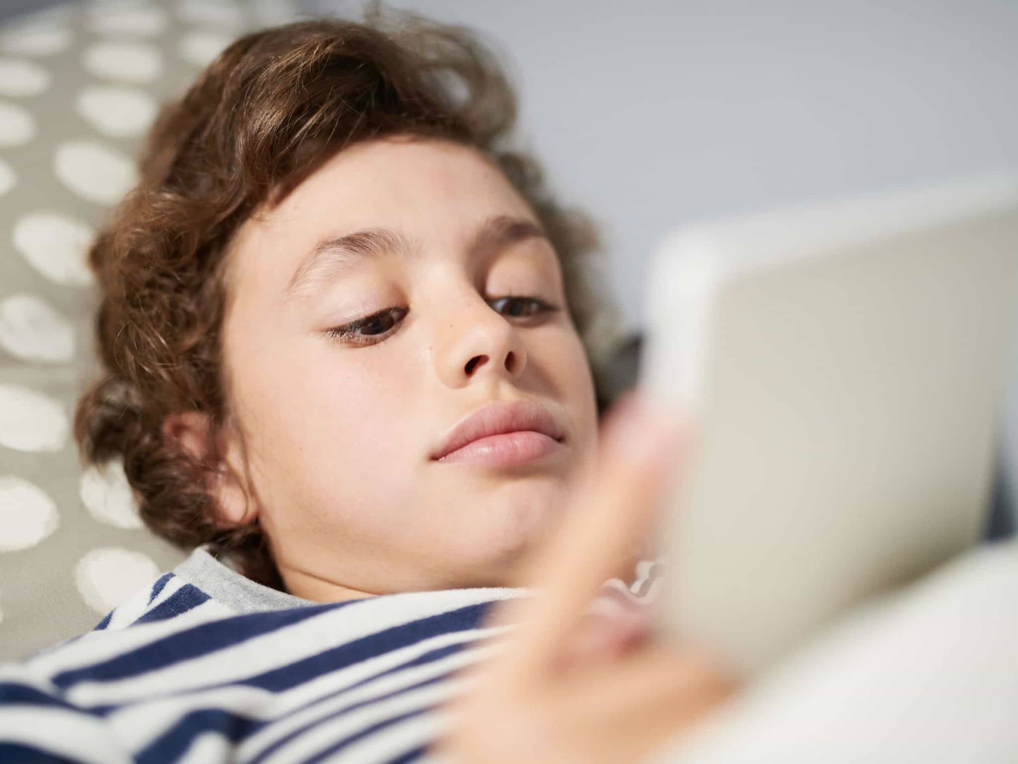 Internetsucht: Liegender Junge guckt auf sein Handy.