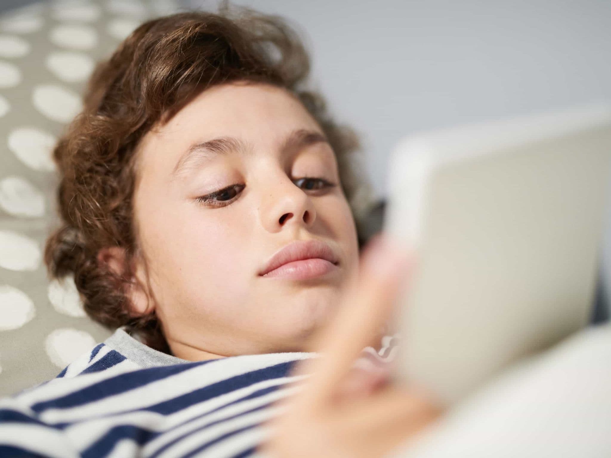 Internetsucht: Liegender Junge guckt auf sein Handy.