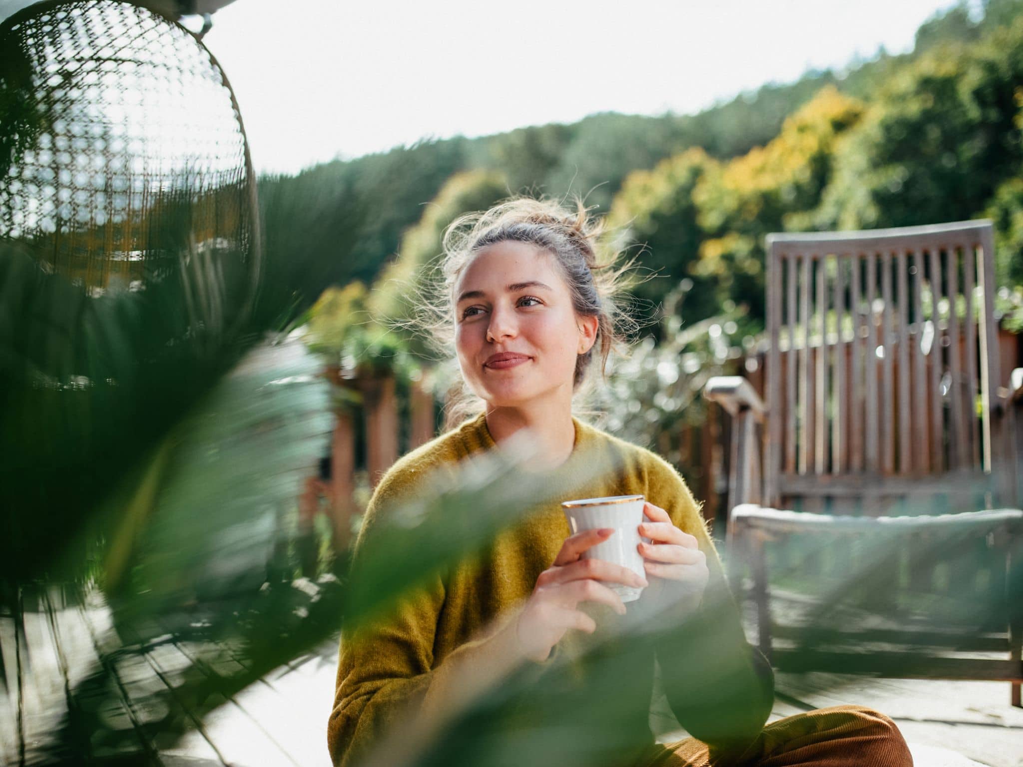 Serotonin erhöhen: Eine Frau sitzt auf einer Terrasse, trinkt Kaffee und lässt sich die Sonne auf die Nase kitzeln