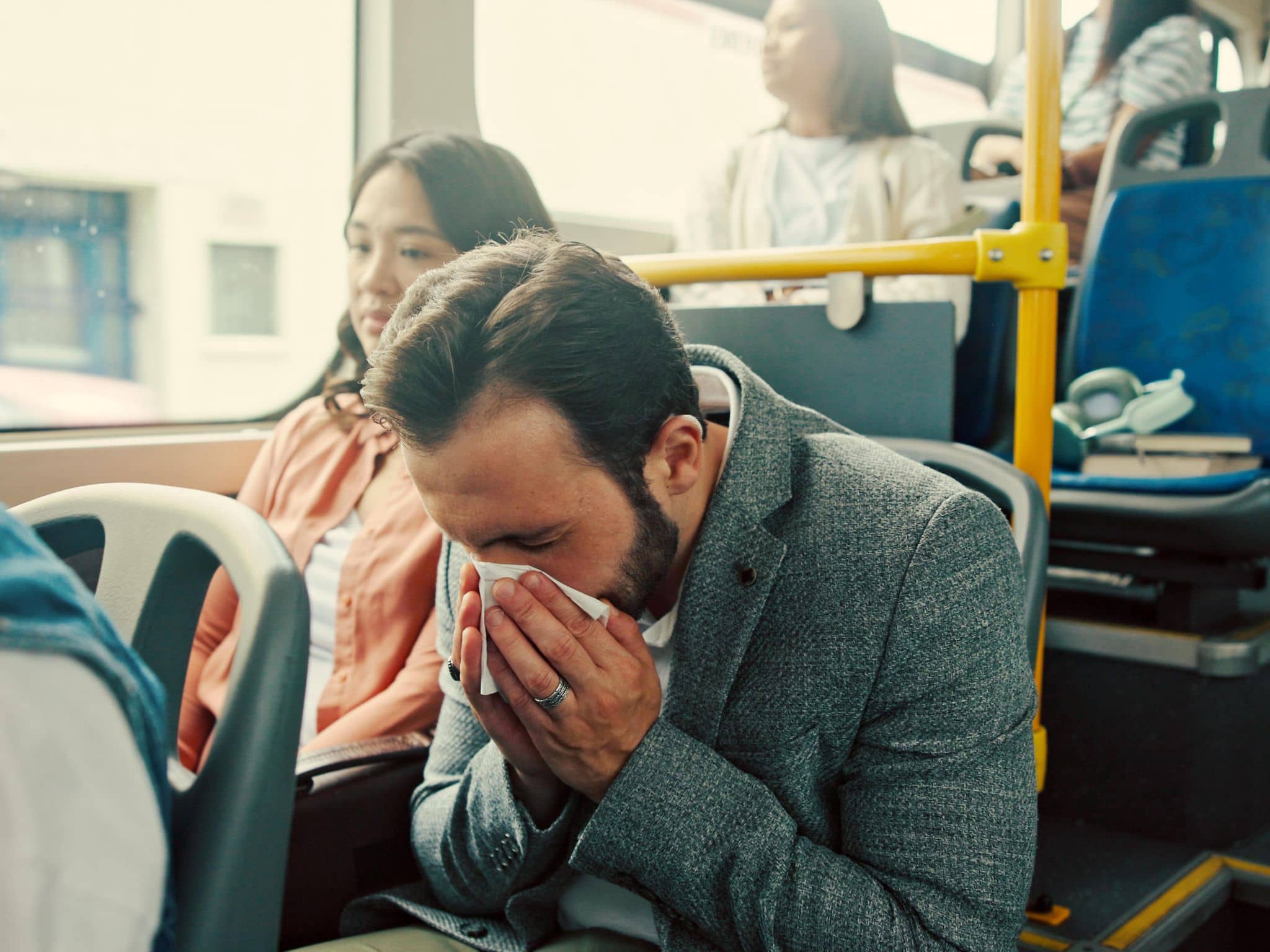 Ein Mann ist erkältet im Bus und fragt sich, wie lange er mit Erkältung wohl ansteckend ist.