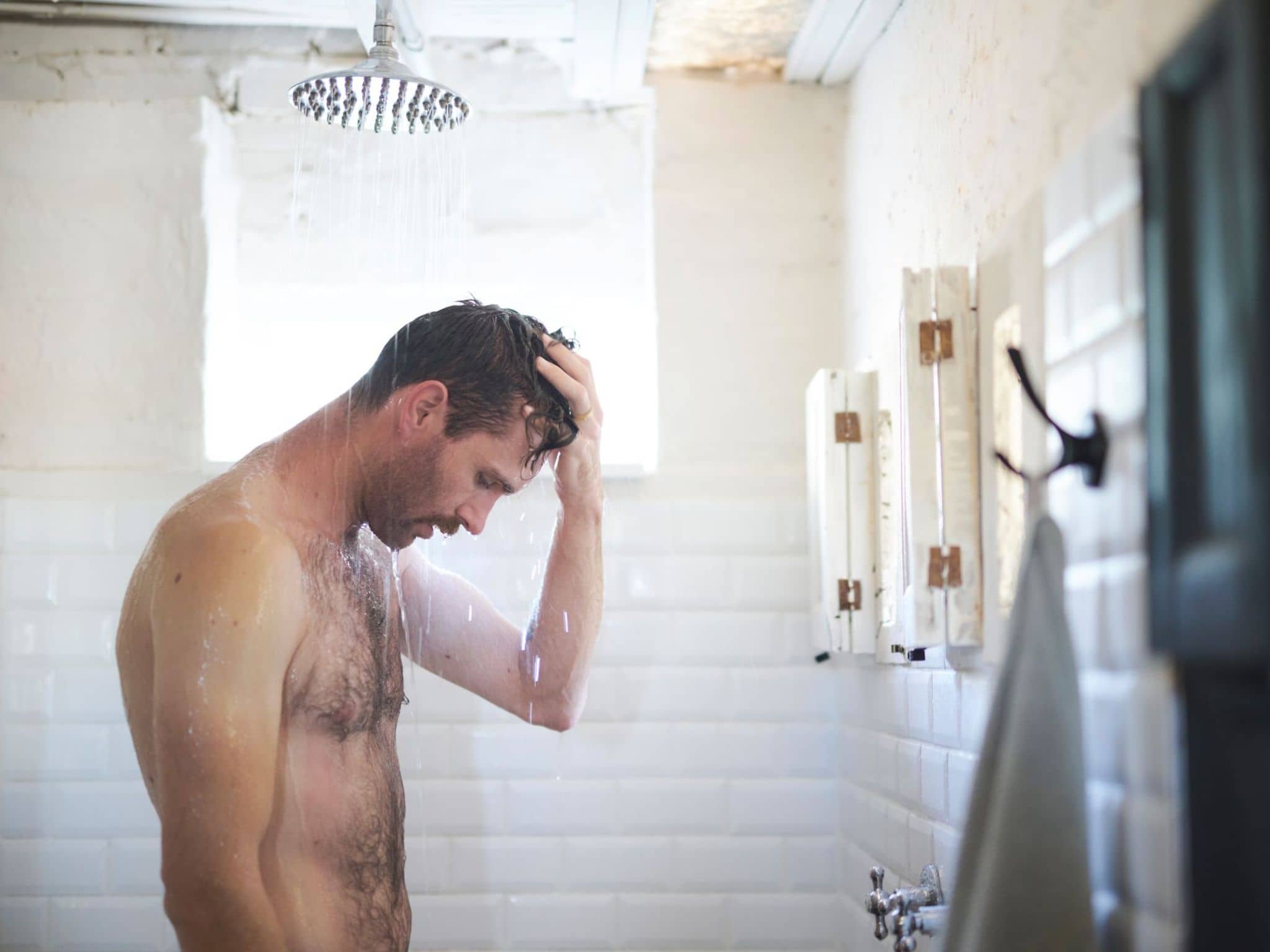 Ein Mann steht unter der Dusche und tastet seine Hoden ab.