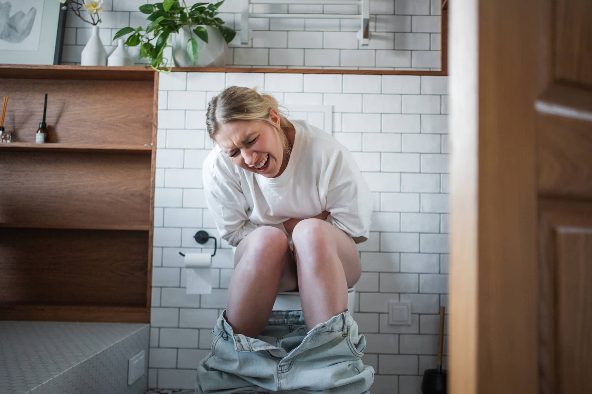 Eine junge Frau sitzt auf der Toilette und krümmt sich vor Schmerzen