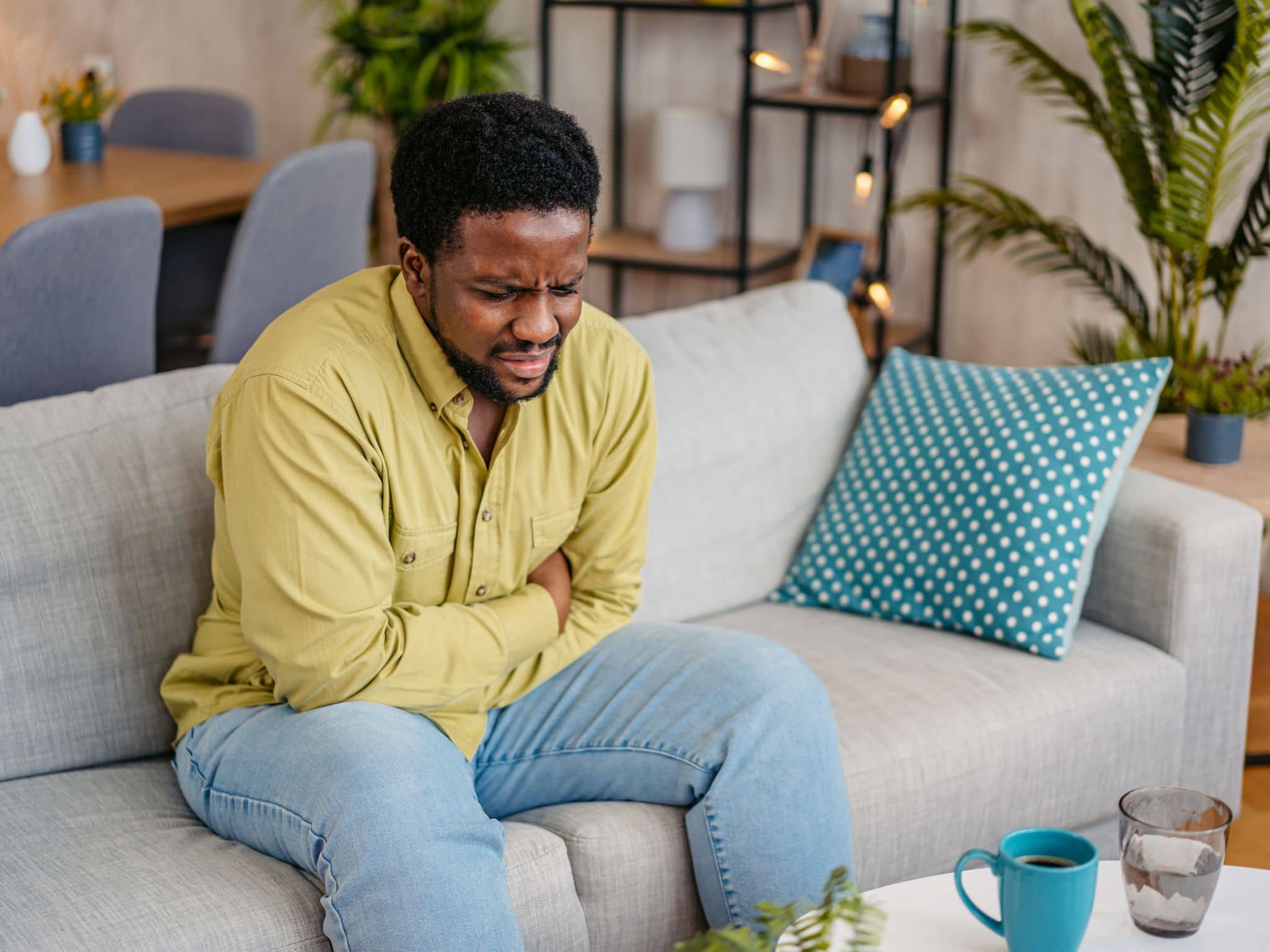 Ein Mann sitzt mit schmerzverzerrtem Gesicht auf einem Sofa und hält sich den Bauch.