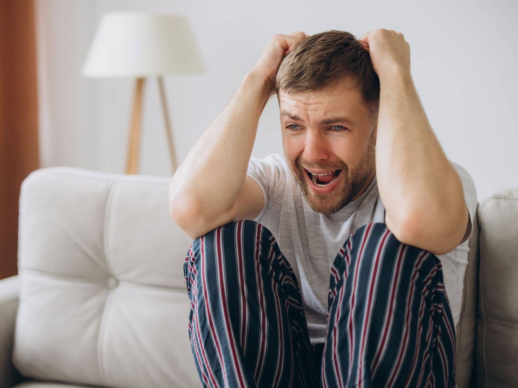 Ein Mann im Pyjama sitzt auf dem Sofa und schreit während einer Psychose.