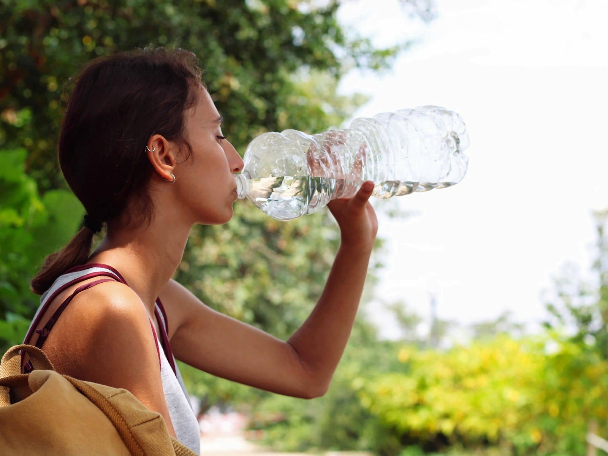 Frau sitzt im Freien und trinkt Wasser aus einer großen Plastikflasche.