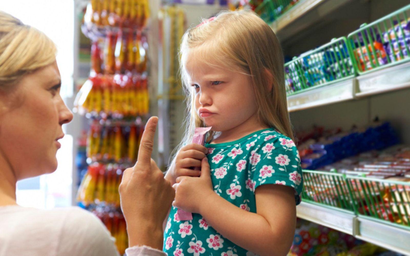 Wut in der Erziehung: Eine Mutter schimpft mit ihrer kleinen Tochter vor dem Süßigkeitenregal eines Supermarkts