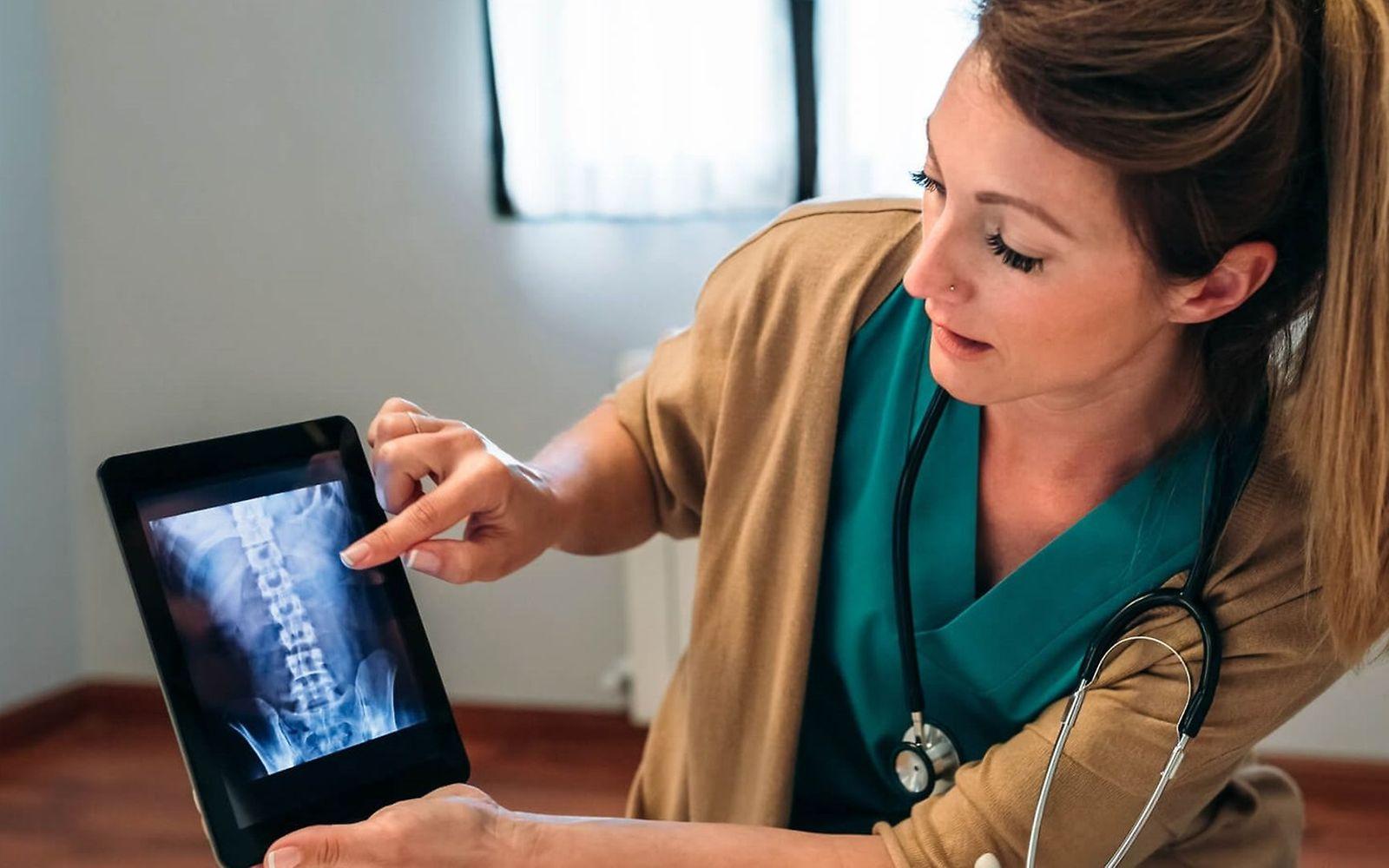 Wichtige Mineralstoffe: Ärztin zeigt das Röntgenbild von einer Wirbelsäule auf dem Tablet.
