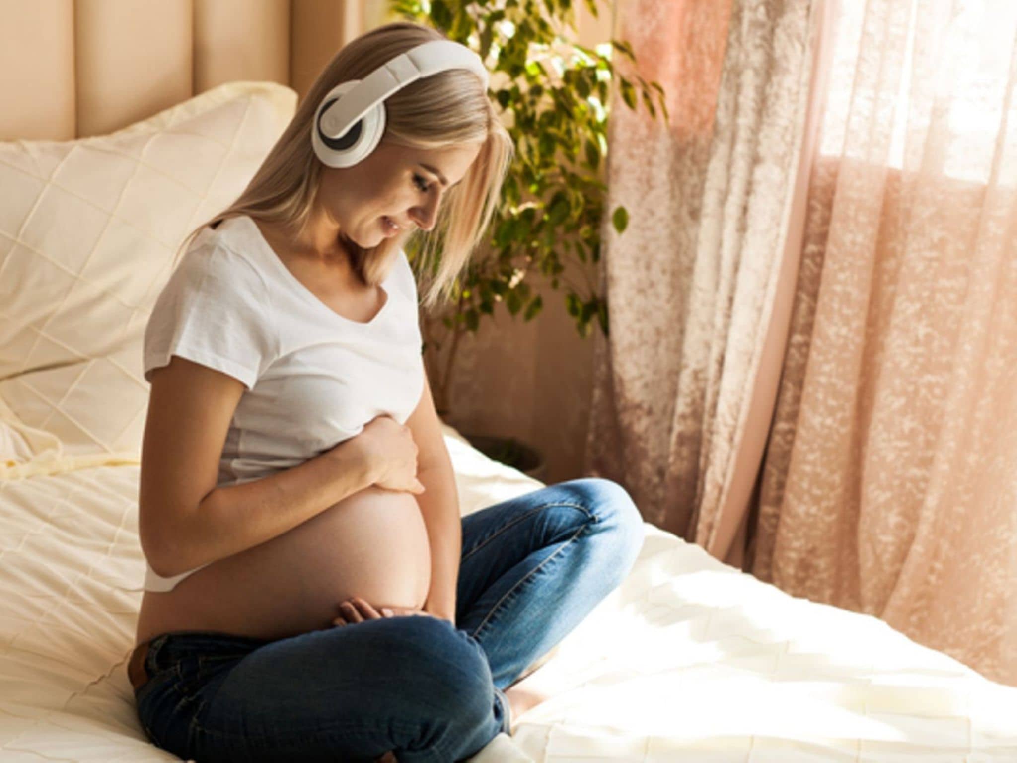 Meditation in der Schwangerschaft: Eine schwangere Frau meditiert auf dem Bett sitzend