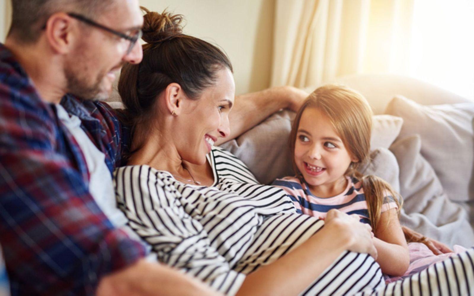 Zweite Schwangerschaft: Schwangere Frau sitzt mit Mann und kleiner Tochter auf dem Sofa