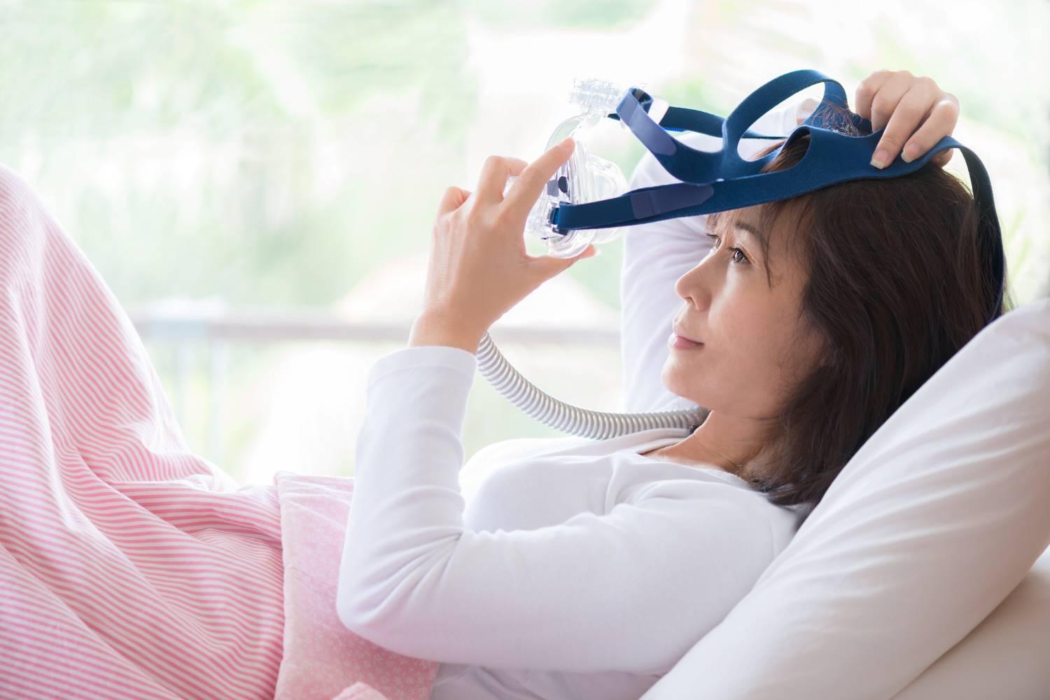 Schlafapnoegeräte: Frau liegt im Bett und setzt sich eine Beatmungsmaske auf.