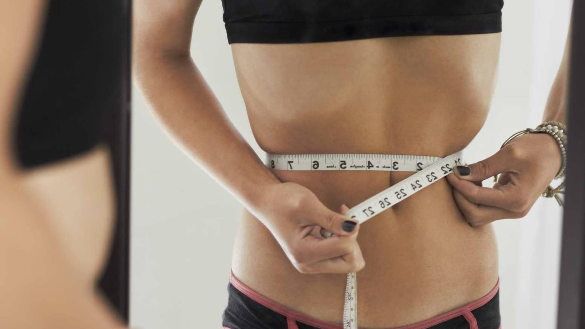 Essstörungen: Sehr dünne Frau misst mit Maßband ihren Taillenumfang.