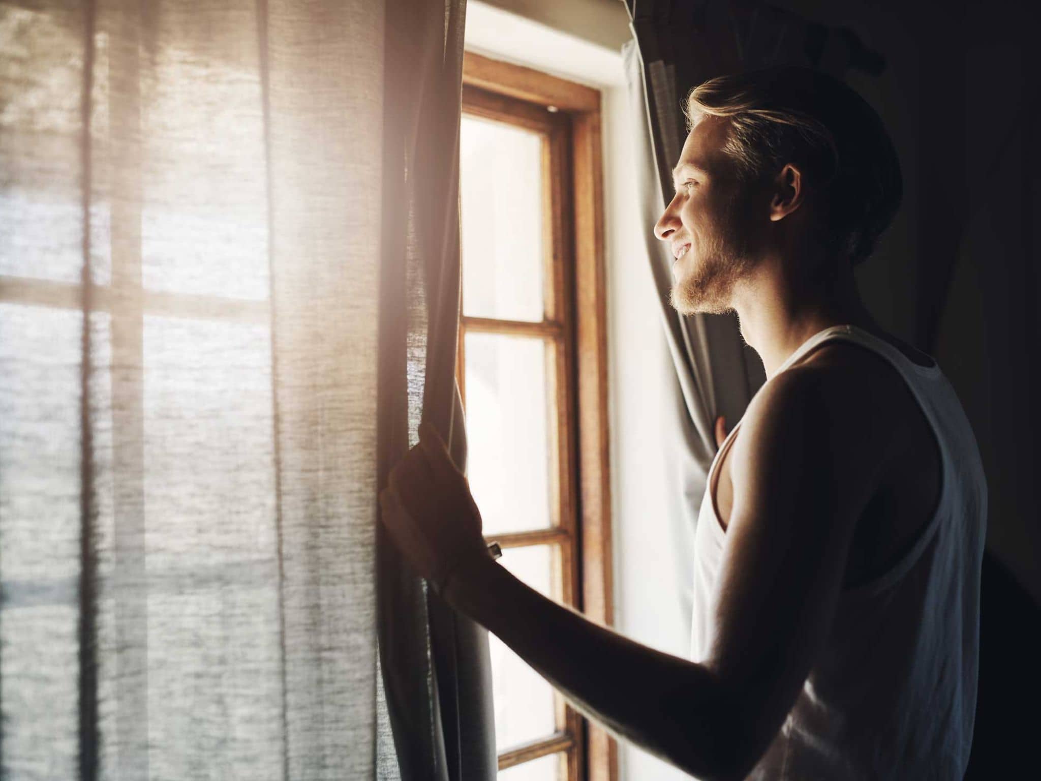 Junger Mann öffent am Morgen die Vorhänge am Fenster