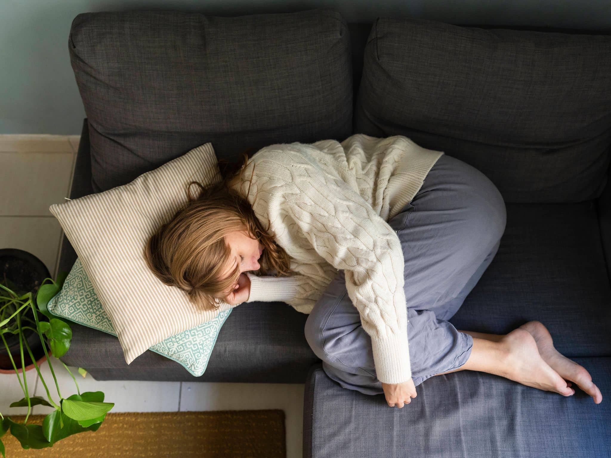 Junge Frau liegt gekrümmt auf der Couch.