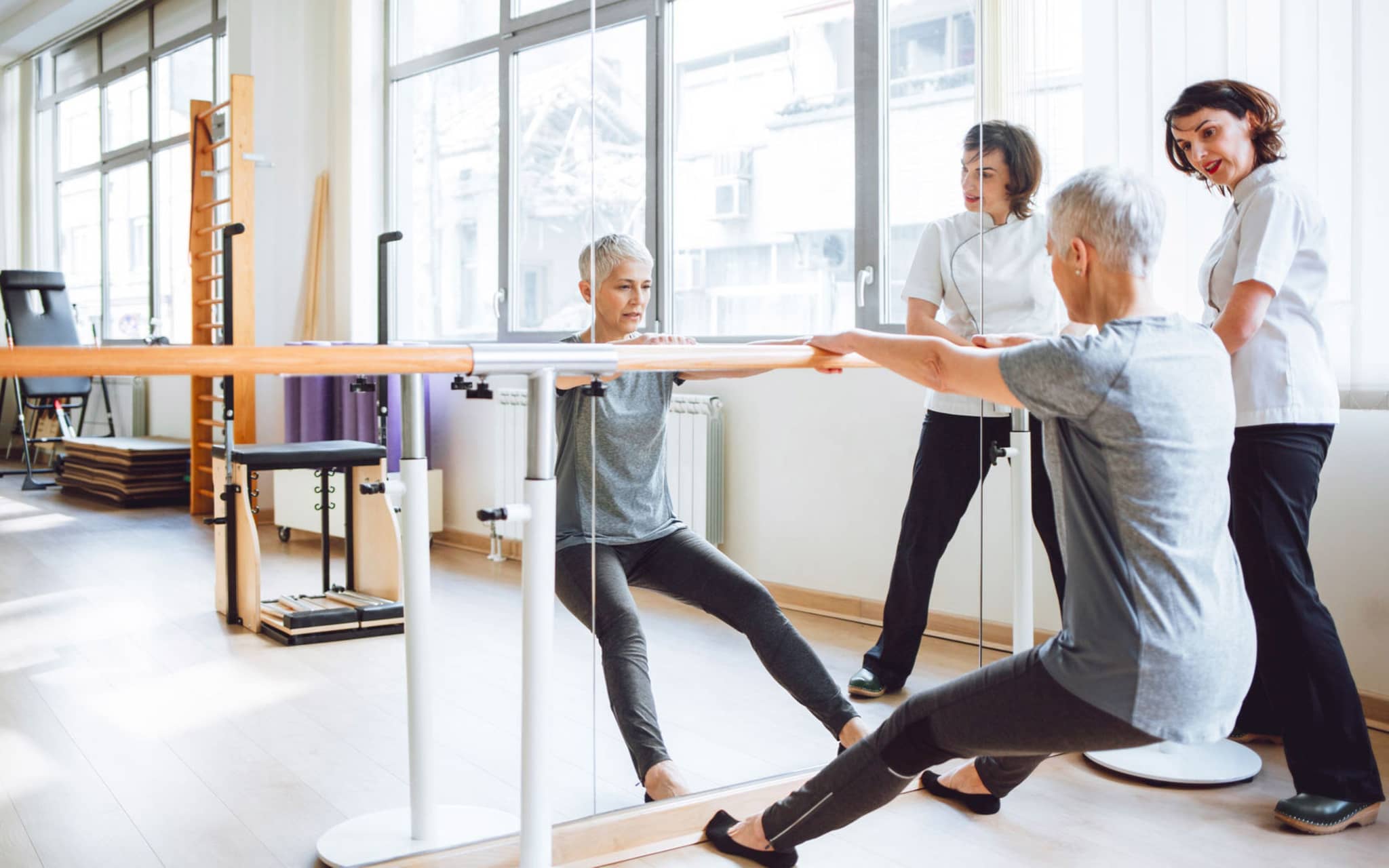 Rehasport: Frau und Trainerin an Stange am Spiegel.