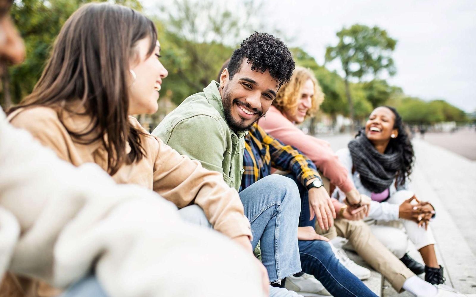 Eine Gruppe junger Leute sitzt im Freien und lacht miteinander