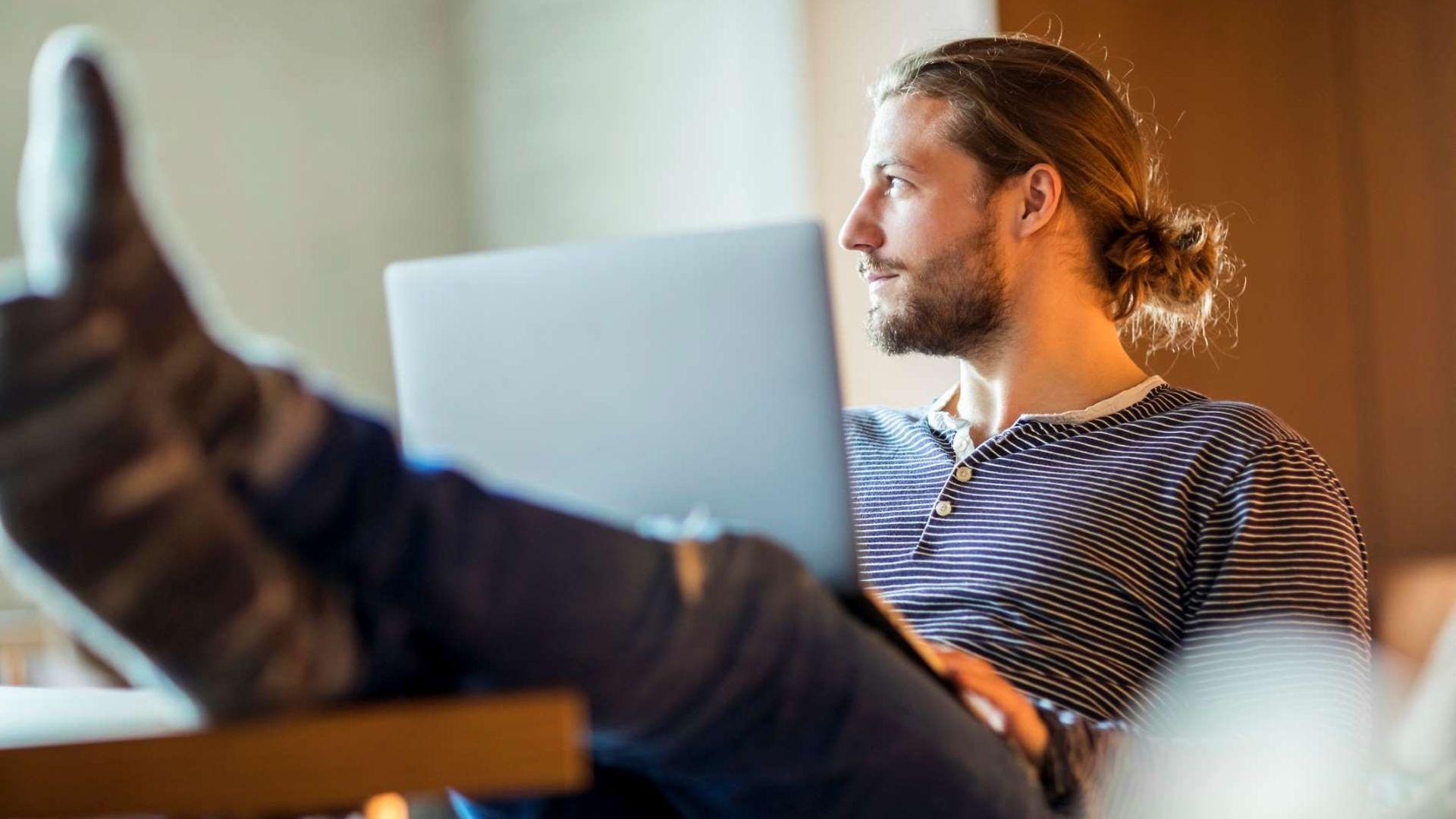 Work-Live-Balance: Mann sitzt in entspannter Pose mit Laptop auf dem Schoß