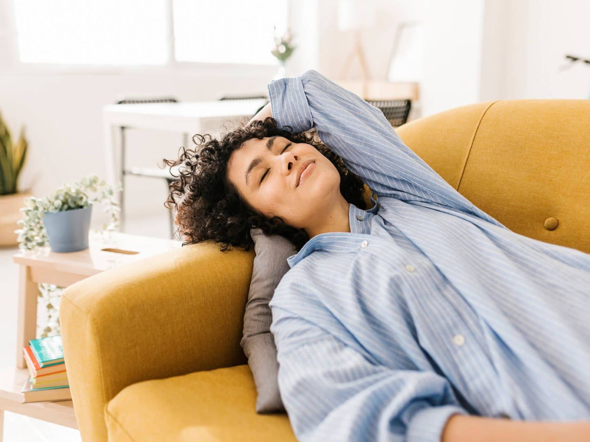 Stressmanagement: Lächelnde Frau liegt entspannt mit geschlossenen Augen auf der Couch.
