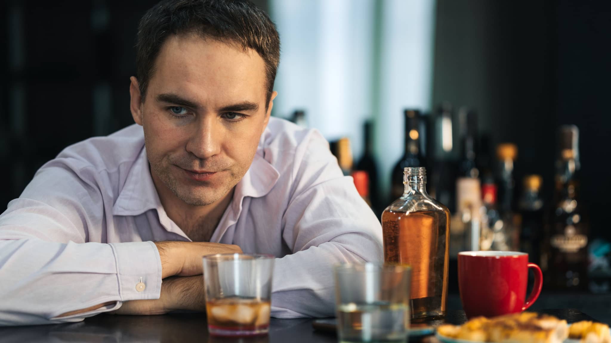 Ein junger Geschäftsmann sitzt an einem Tresen, auf dem viele leere Gläser stehen