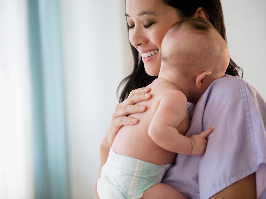 Bild: Asiatische Frau hält ein Baby auf dem Arm und sieht zufrieden aus.