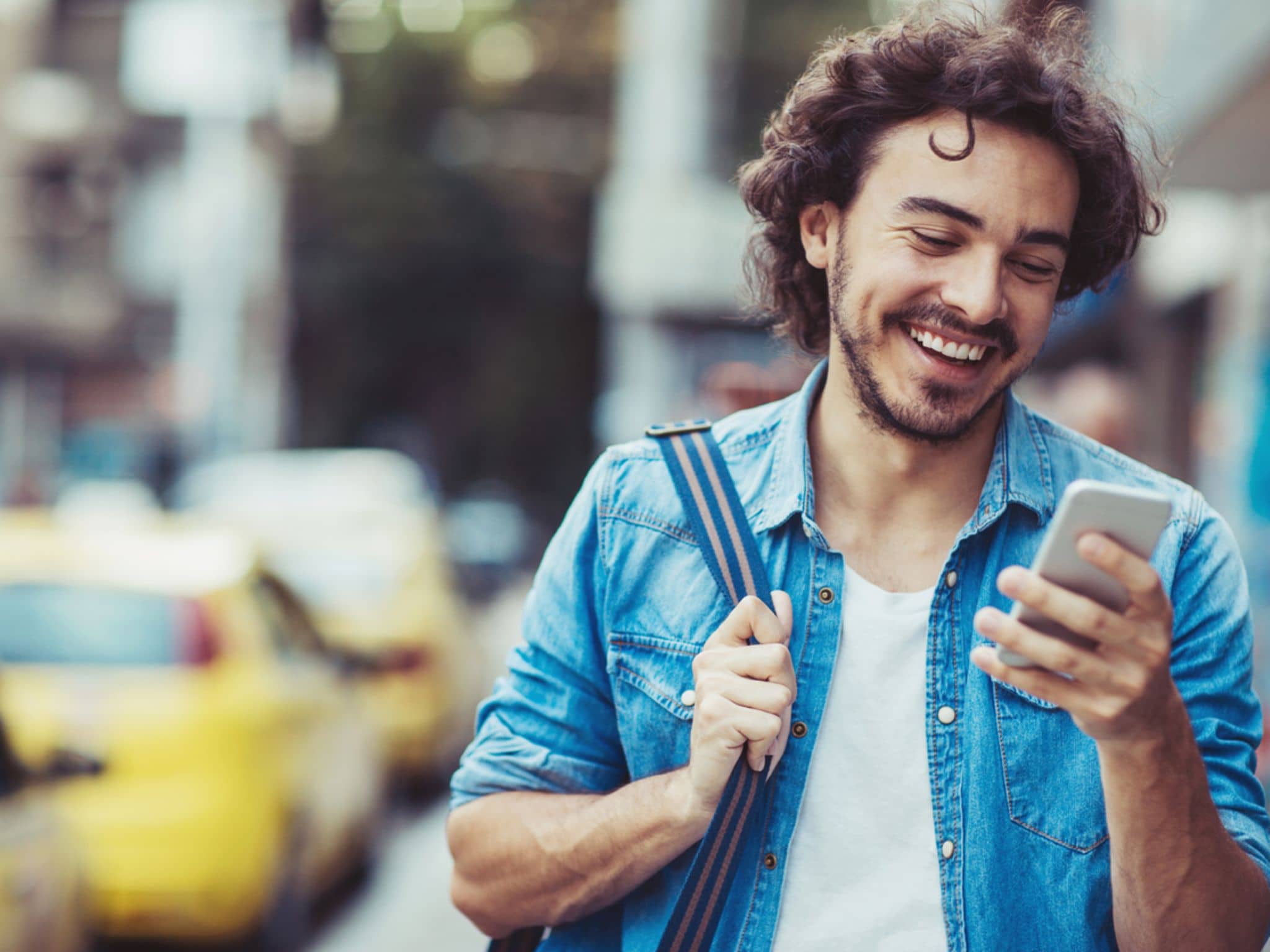 Bild: Junger Mann mit Tasche auf der Schulter schaut auf sein Handy.