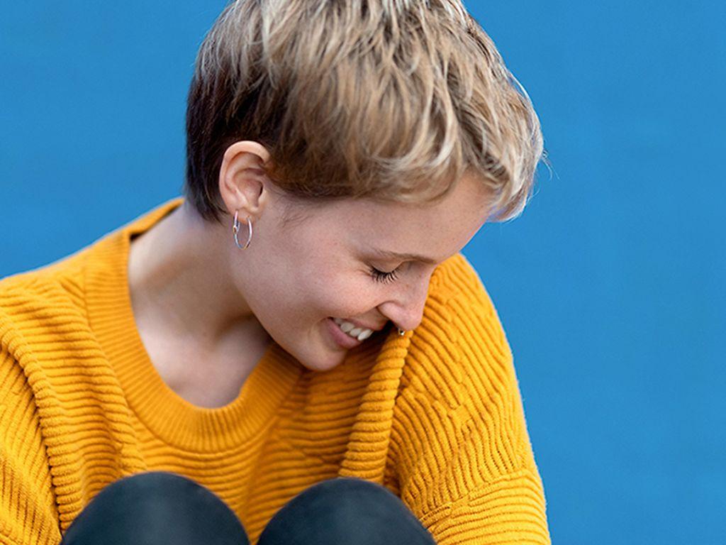 Körpersprache: Junge Frau im gelben Pullover senkt den Kopf schüchtern zur Seite