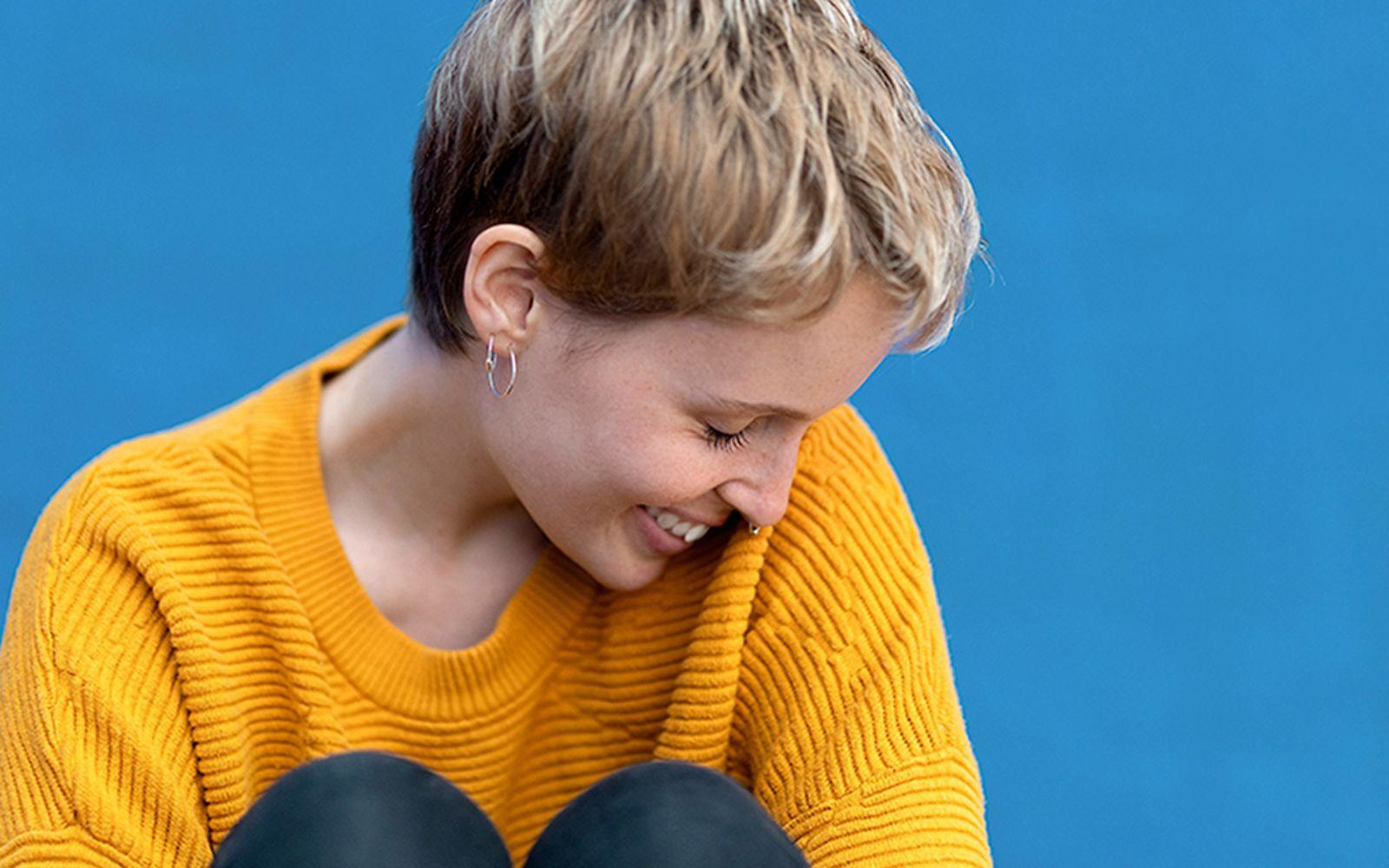 Körpersprache: Junge Frau im gelben Pullover senkt den Kopf schüchtern zur Seite