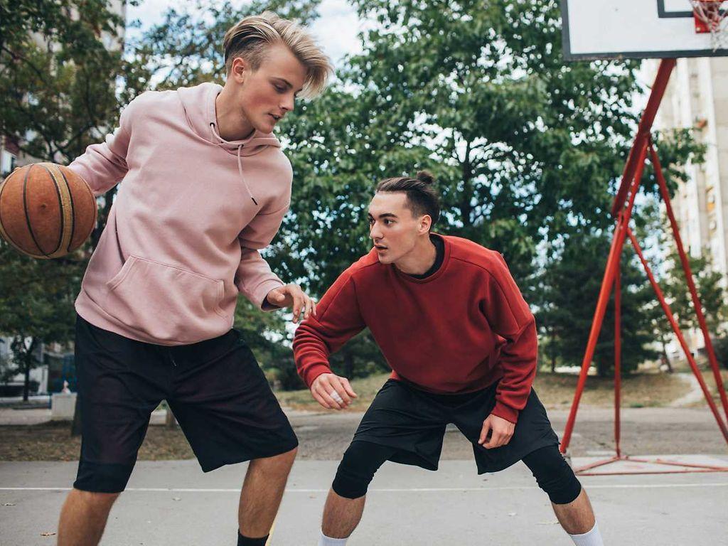 Zwei Jugendliche spielen draußen Basketball