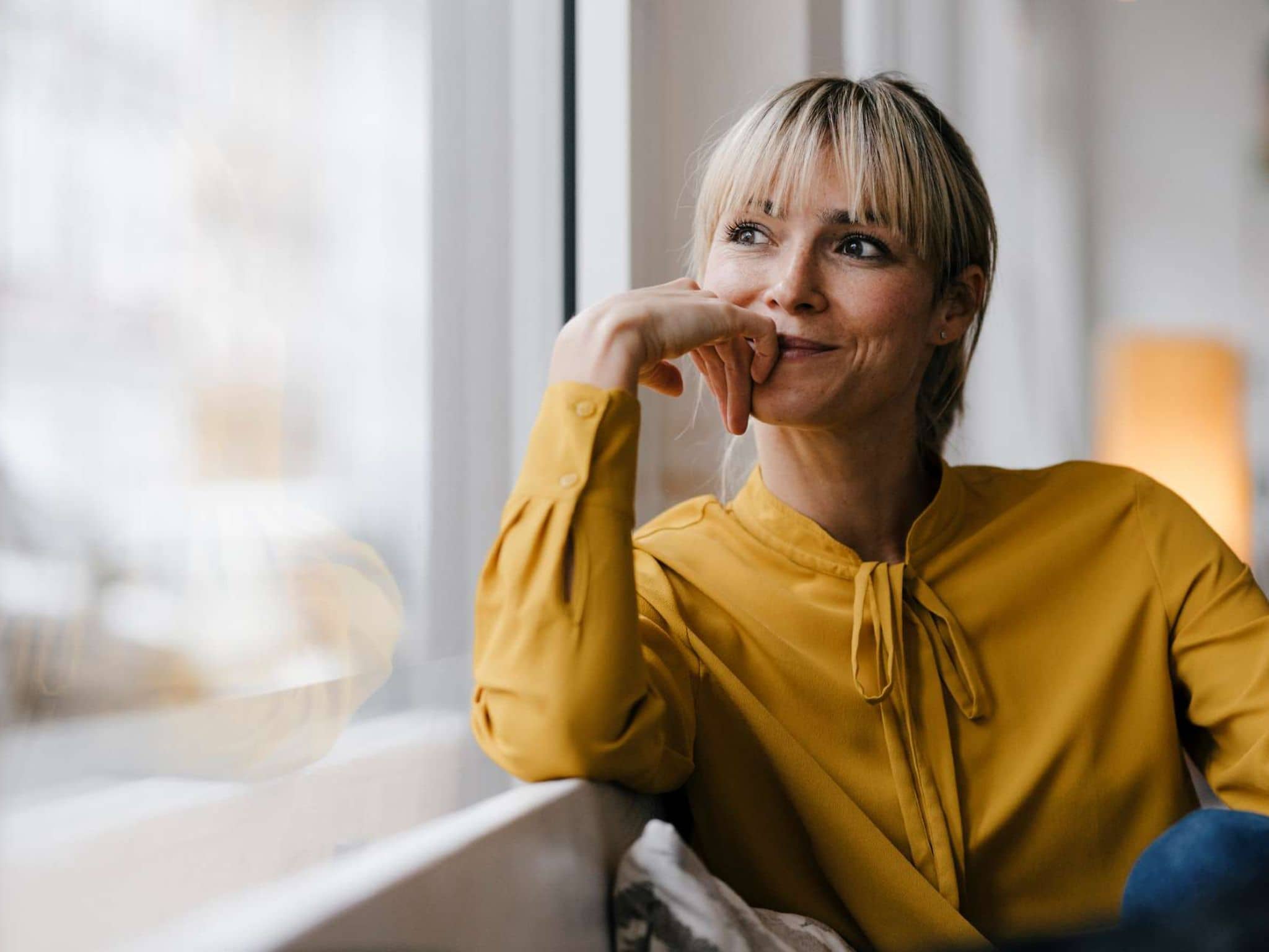Darmkrebsvorsorge: Frau sitzt am Fenster und schaut gedankenverloren hinaus.