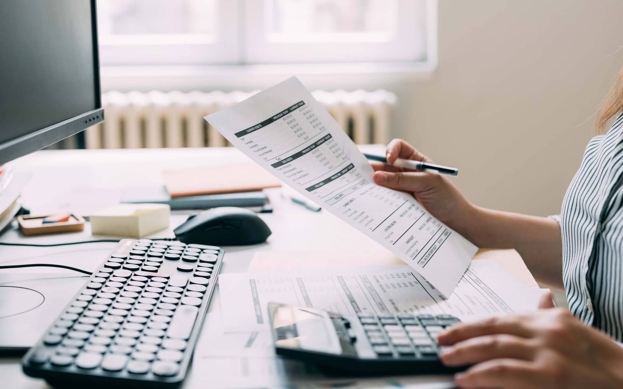 Symbolfoto Abrechnungsbetrug: Frau am PC mit Rechnungen in der Hand.