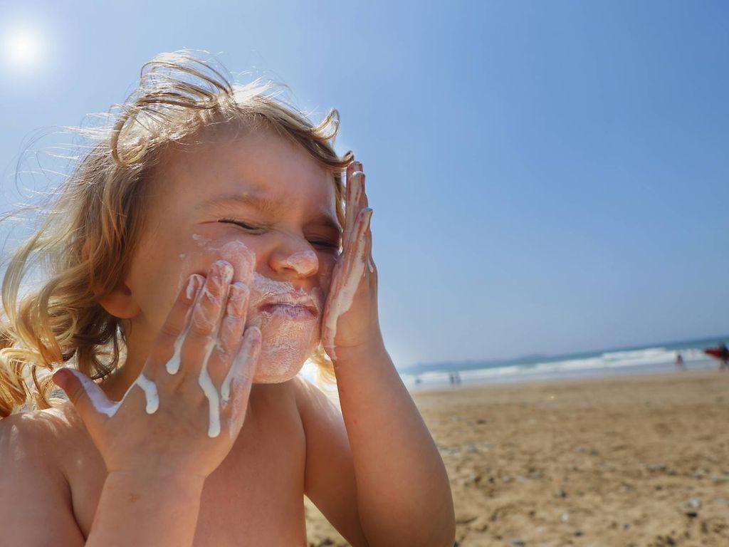 Sonnenbrand bei Kindern: Kleines Mädchen cremt sich am Strand das Gesicht ein